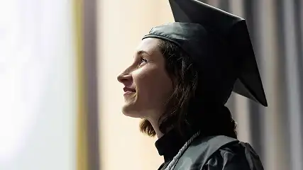 Central Piedmont student in graduation cap and gown smiling and gazing into distance.