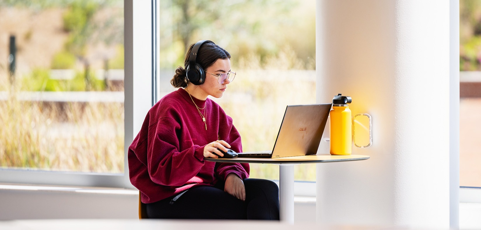 Central Piedmont student wearing headphones while working on laptop in open, airy room on campus.