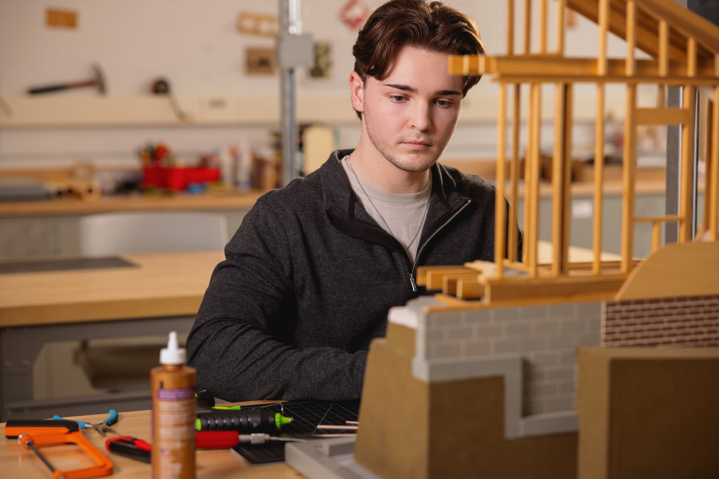Central Piedmont student in shop, surrounding by building materials, assembling timber scale model of building.