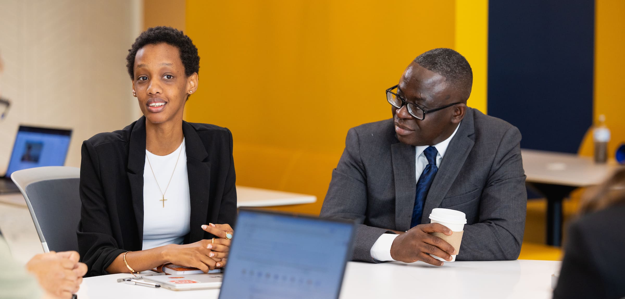 Two professionals in business dress talking across a meeting table