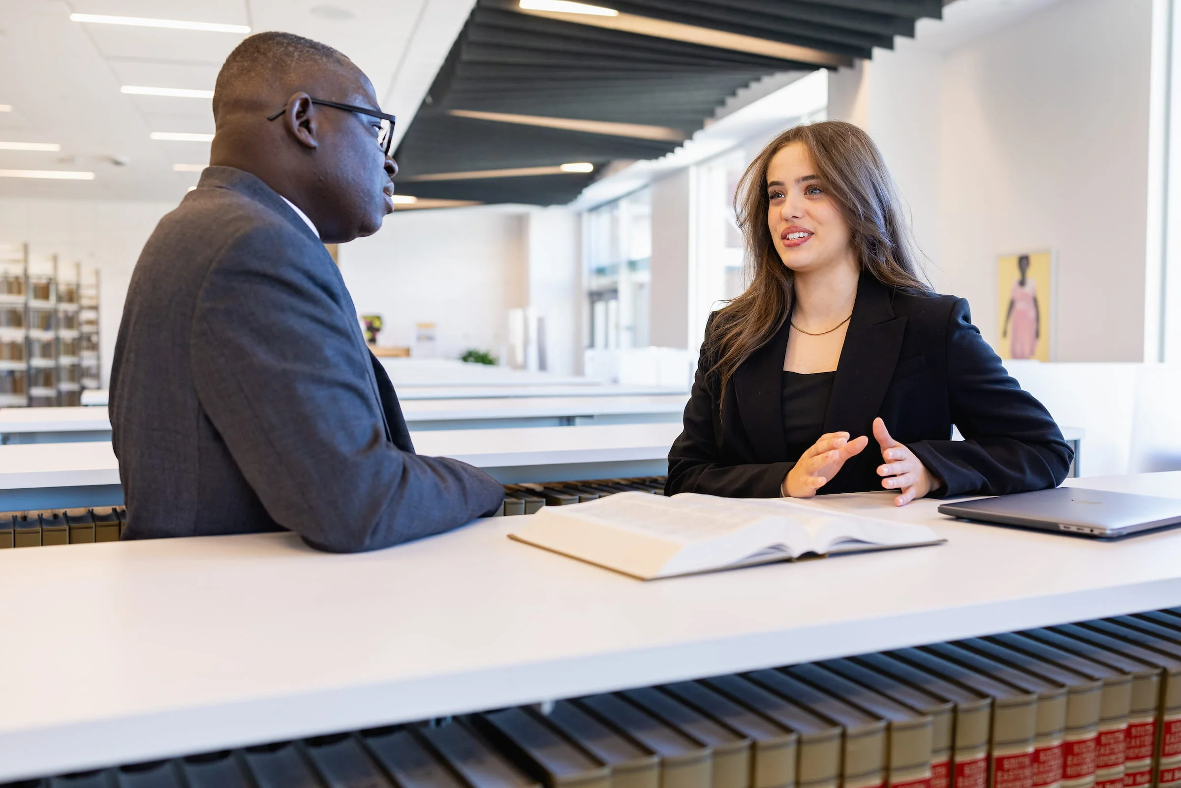 Two business students in professional dress talking across a desk