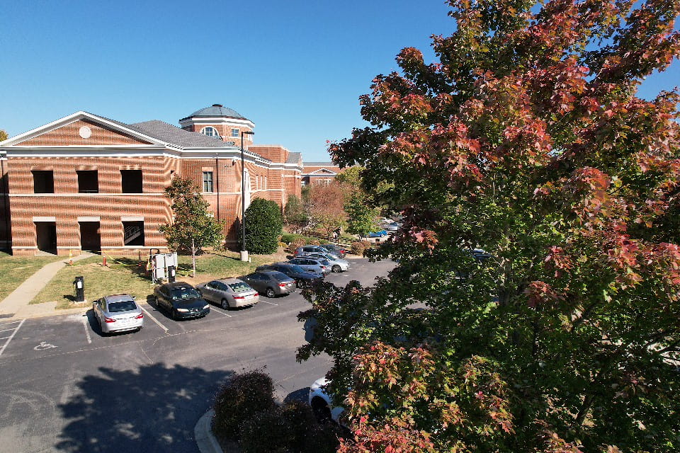 Aerial of Central Piedmont campus parking lot and brick building with large tree sporting fall foliage in foreground.