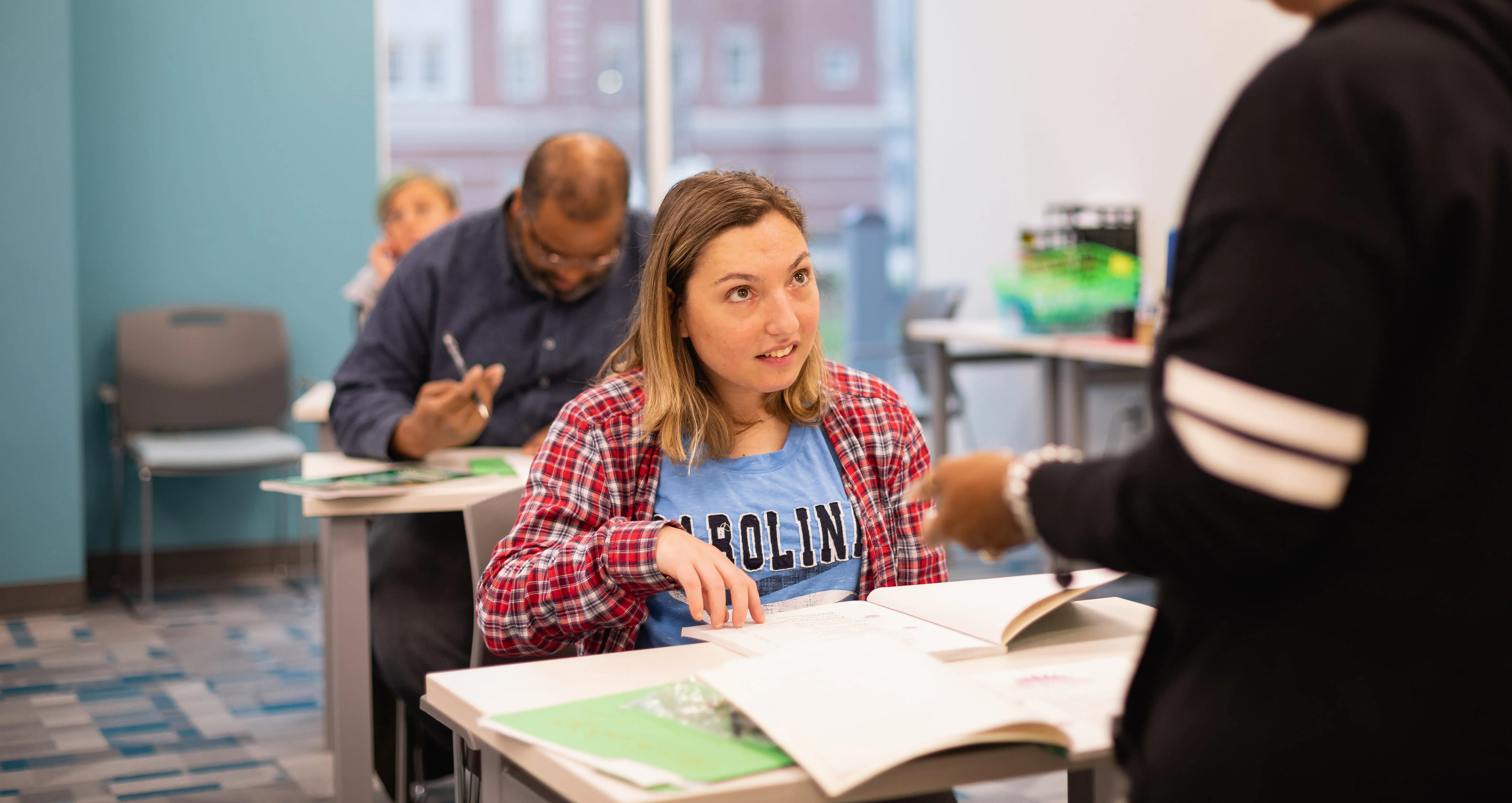 Student at a desk with an open textbook talking with an instructor
