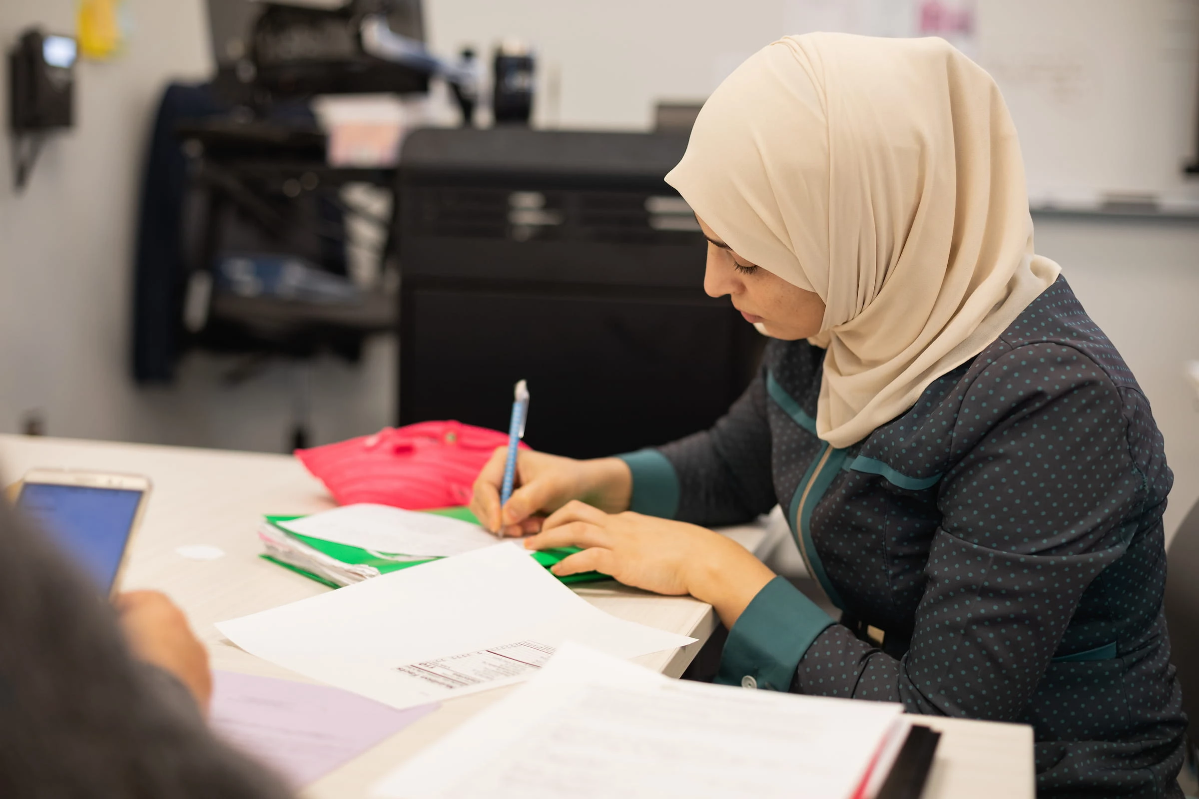 Student in a hijab writing notes at a desk