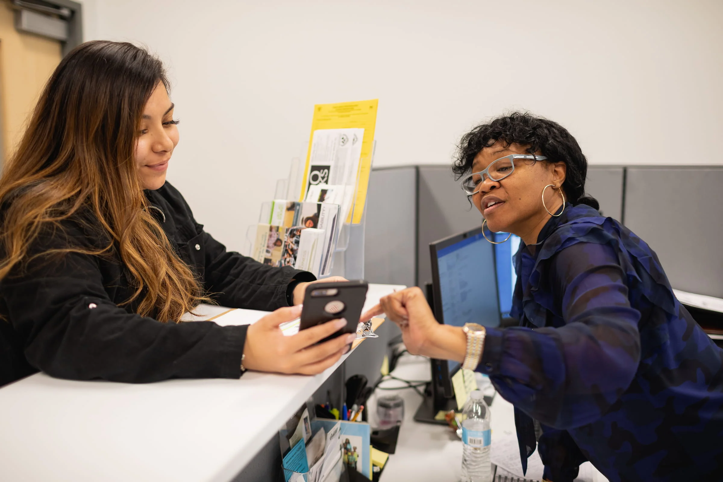 Student showing a phone to a staff member at an office desk