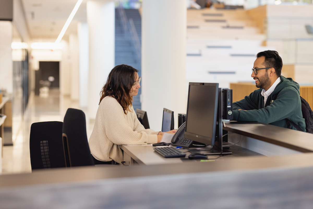 Student working at a help desk, assisting another student