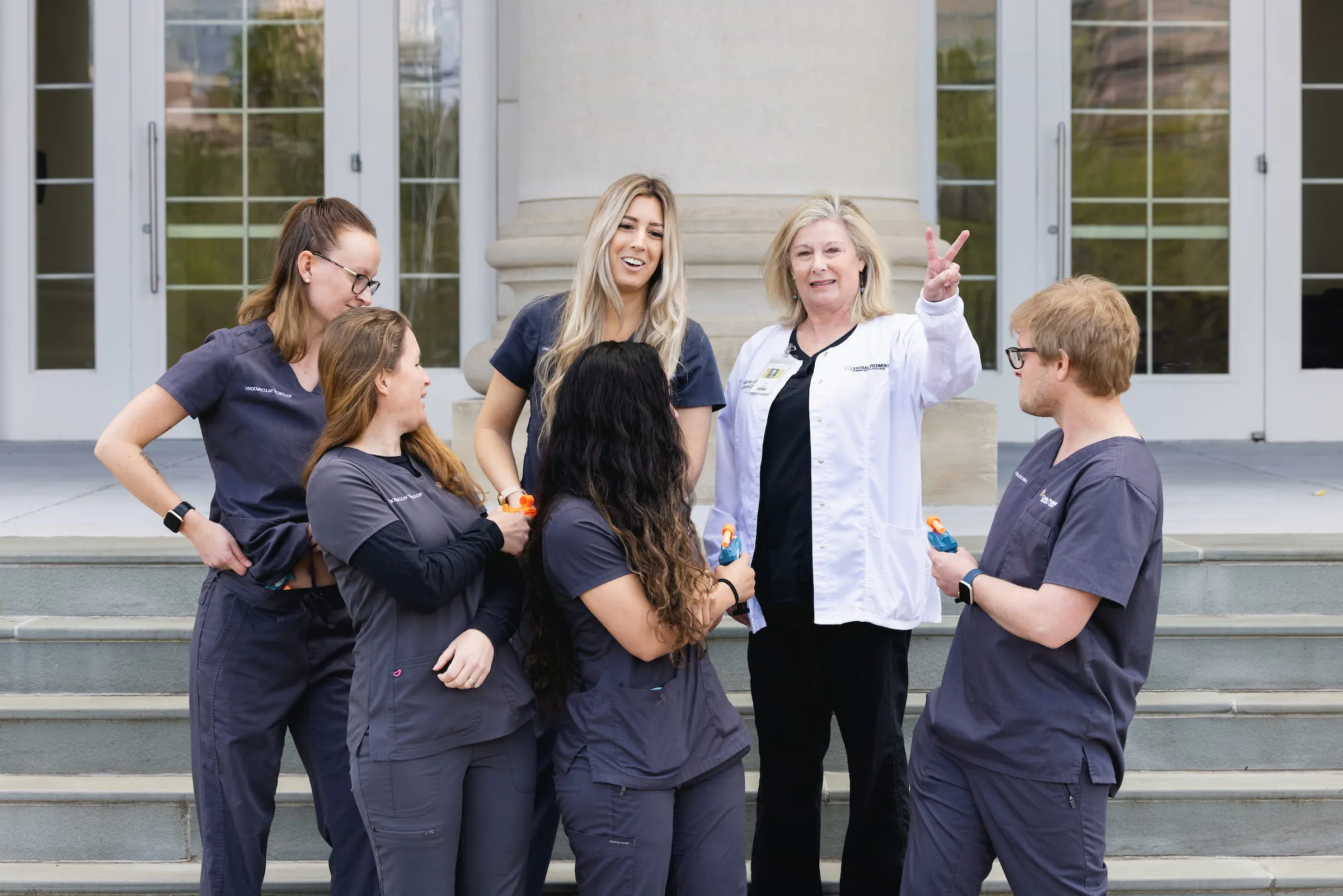 Instructor in a white coat talking with students in scrubs outside a campus building