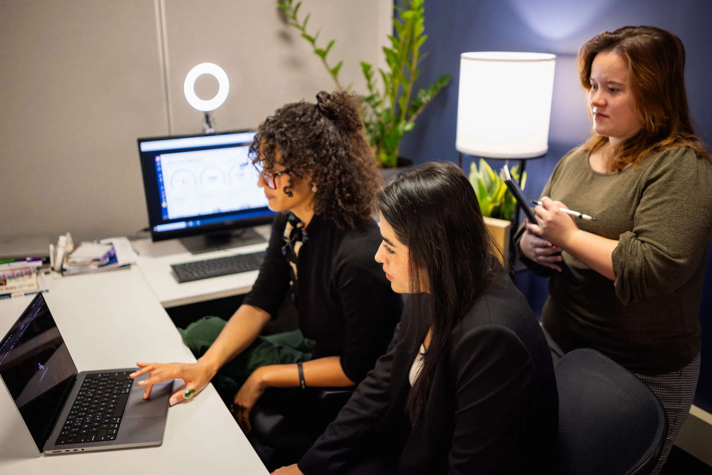 Three colleagues reviewing work together at a desk monitor
