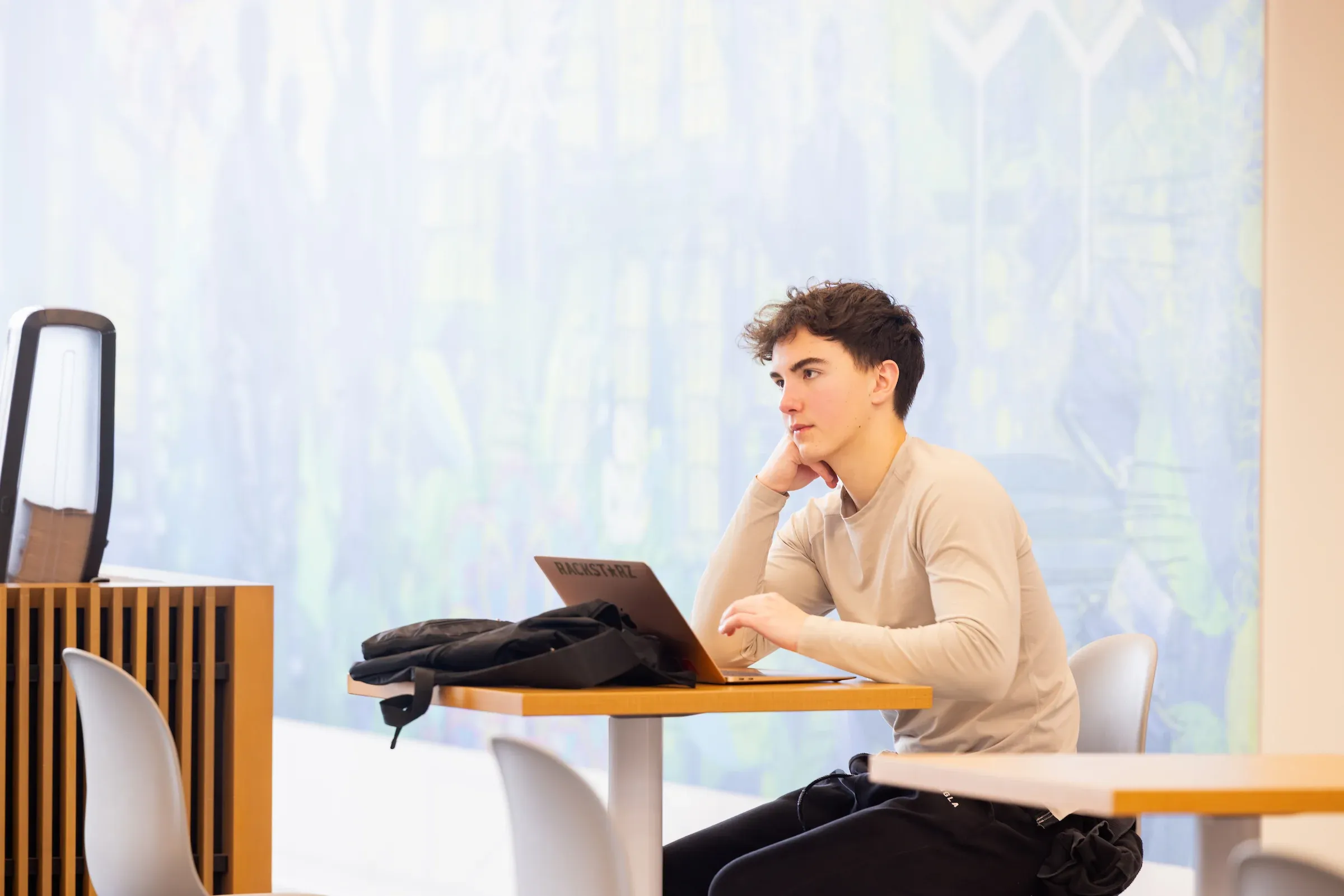 Student working at a laptop beside a bright window