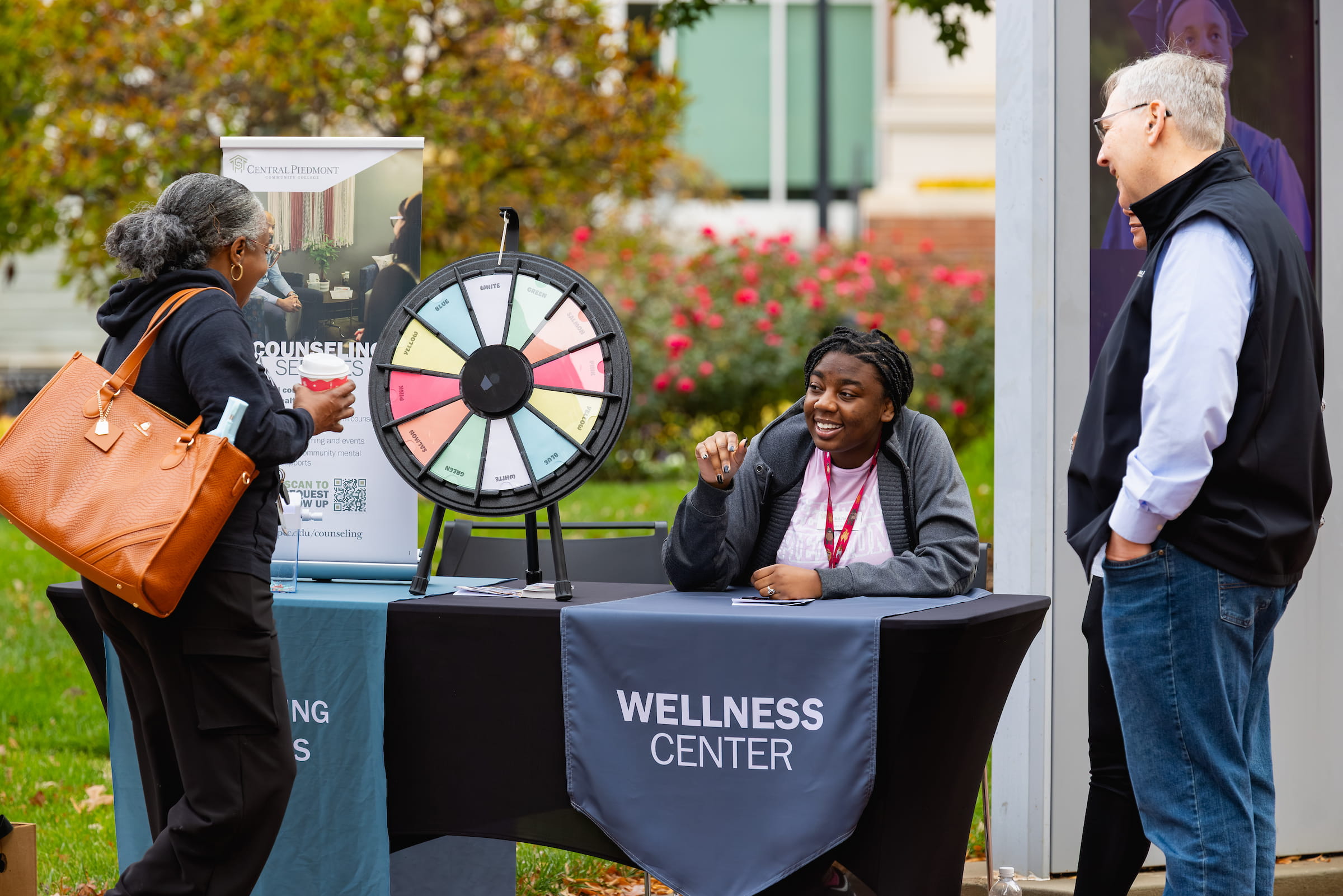 Staff at a Wellness Center table with a prize wheel at an outdoor event