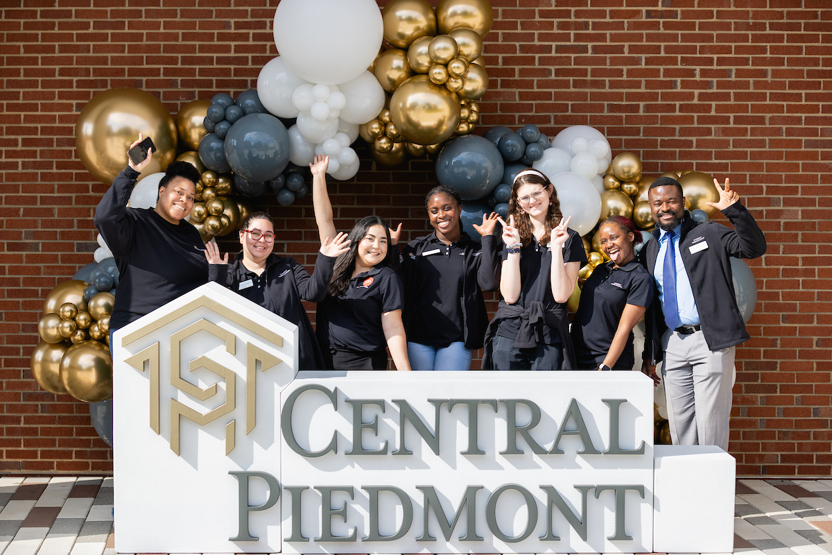 Group of student ambassadors standing in front of a Central Piedmont sign