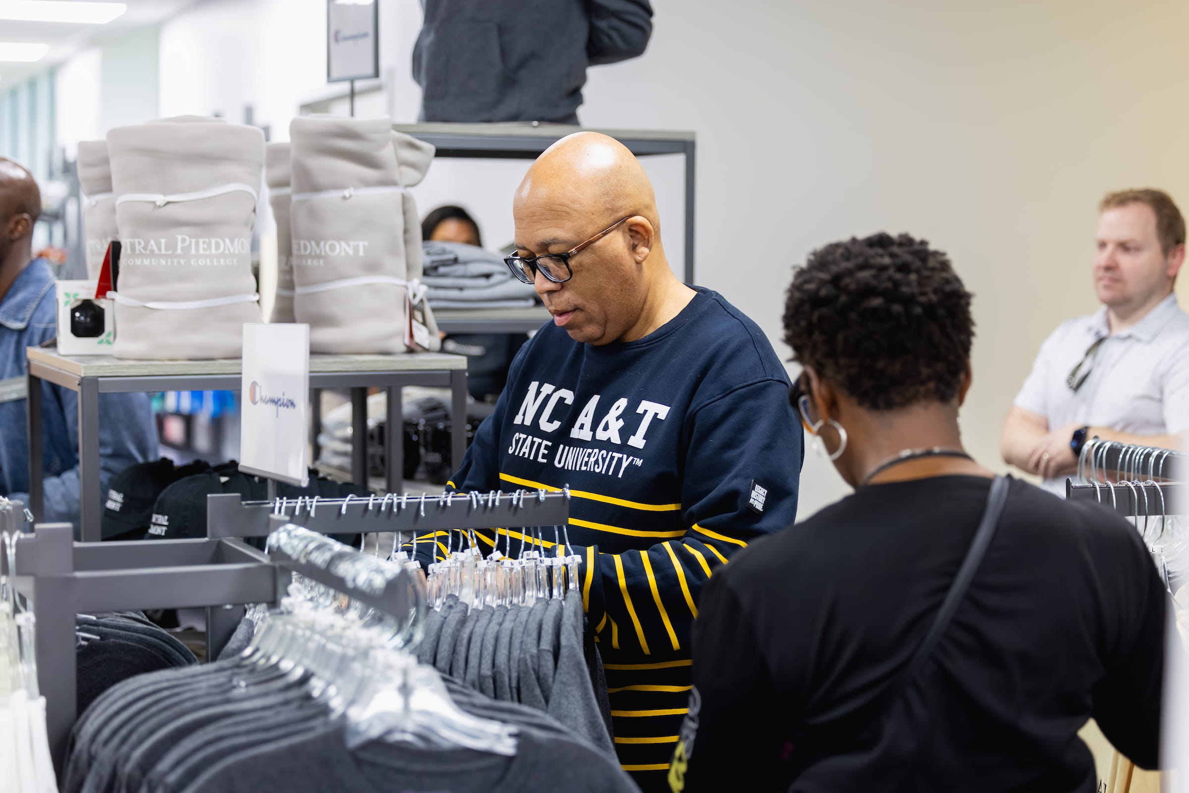 People looking at T-shirts, hats, blankets, and other Central Piedmont apparel inside campus store.