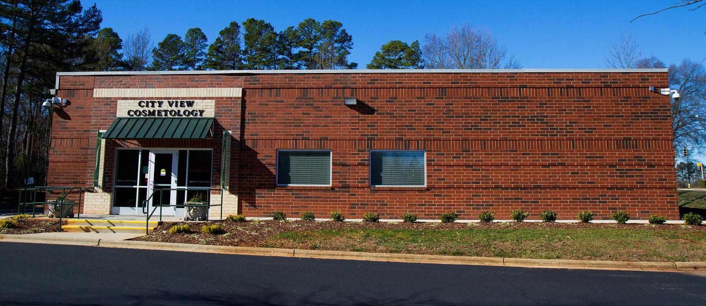 Exterior of one-story brick City View Cosmetology center with parking lot in front.