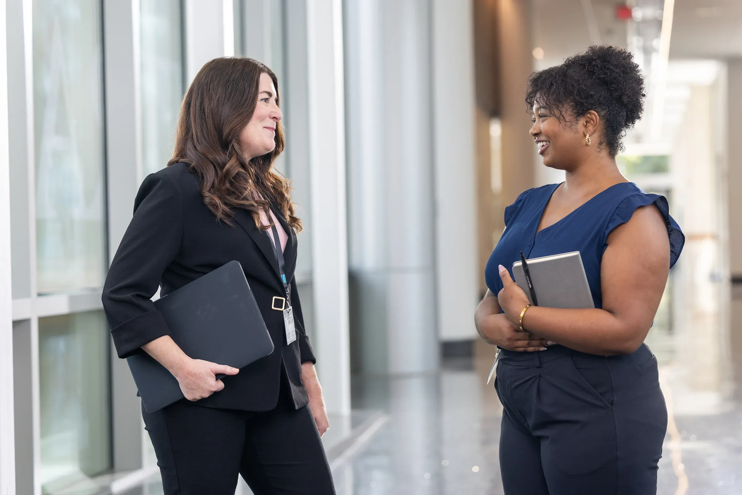 Two students in business dress talking while holding folders