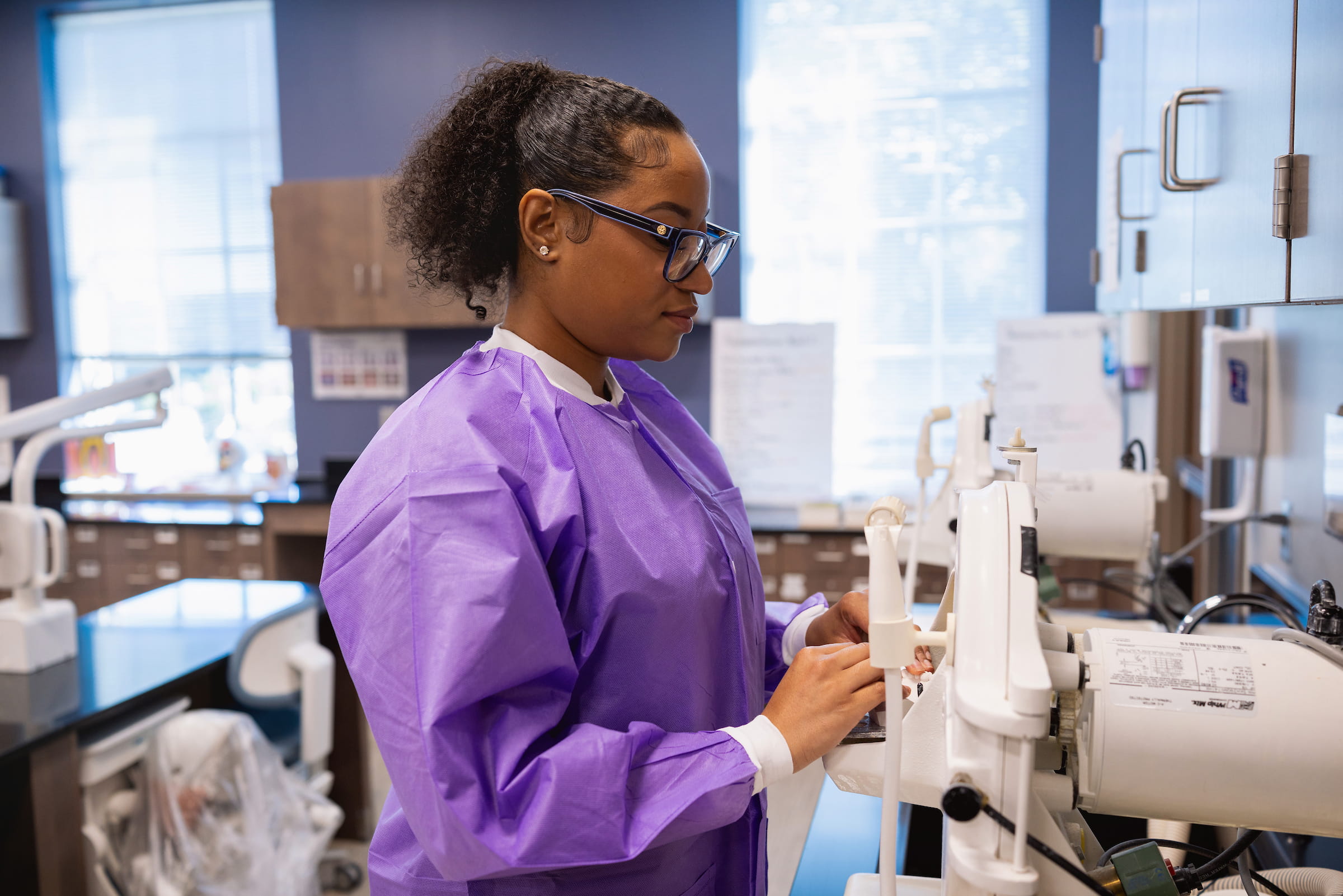 Dental assisting student in a protective gown preparing equipment in a clinic bay