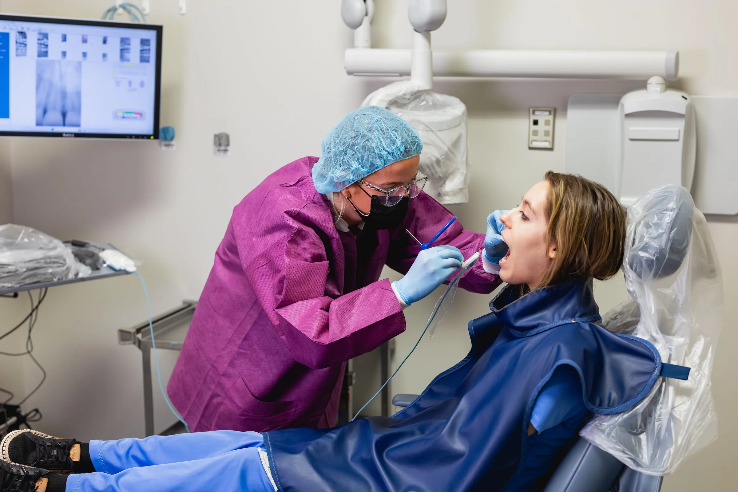 Dental student in protective gear treating a patient in the clinic