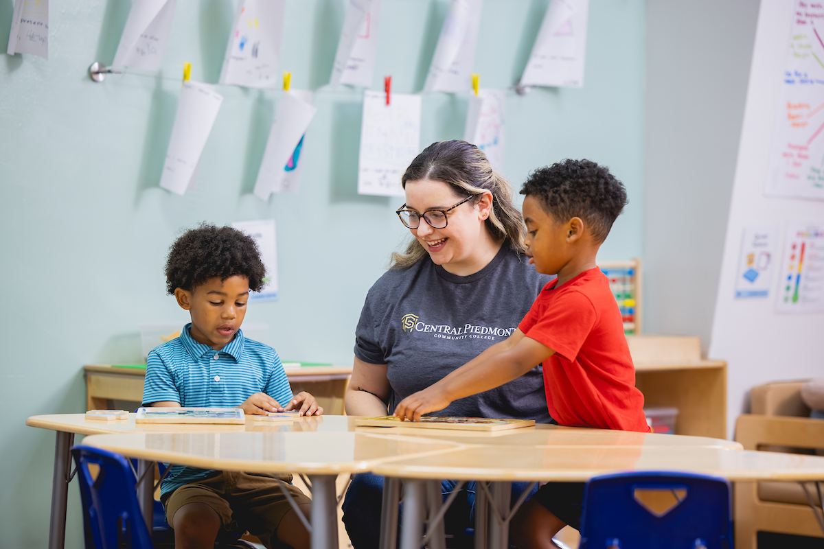Early childhood education program graduate sitting at a table with two young students