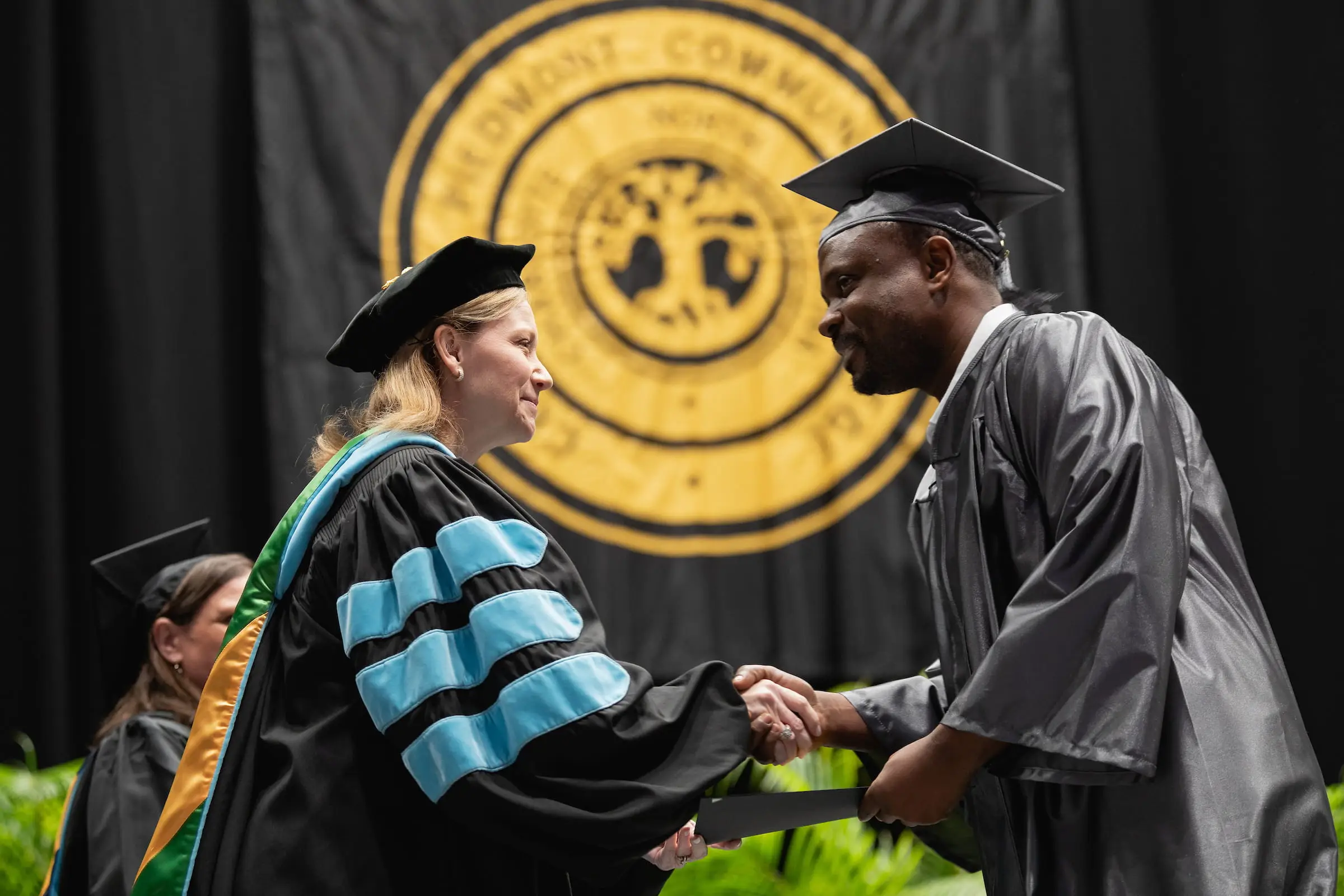 Graduate shaking hands with a faculty member in front of the college seal