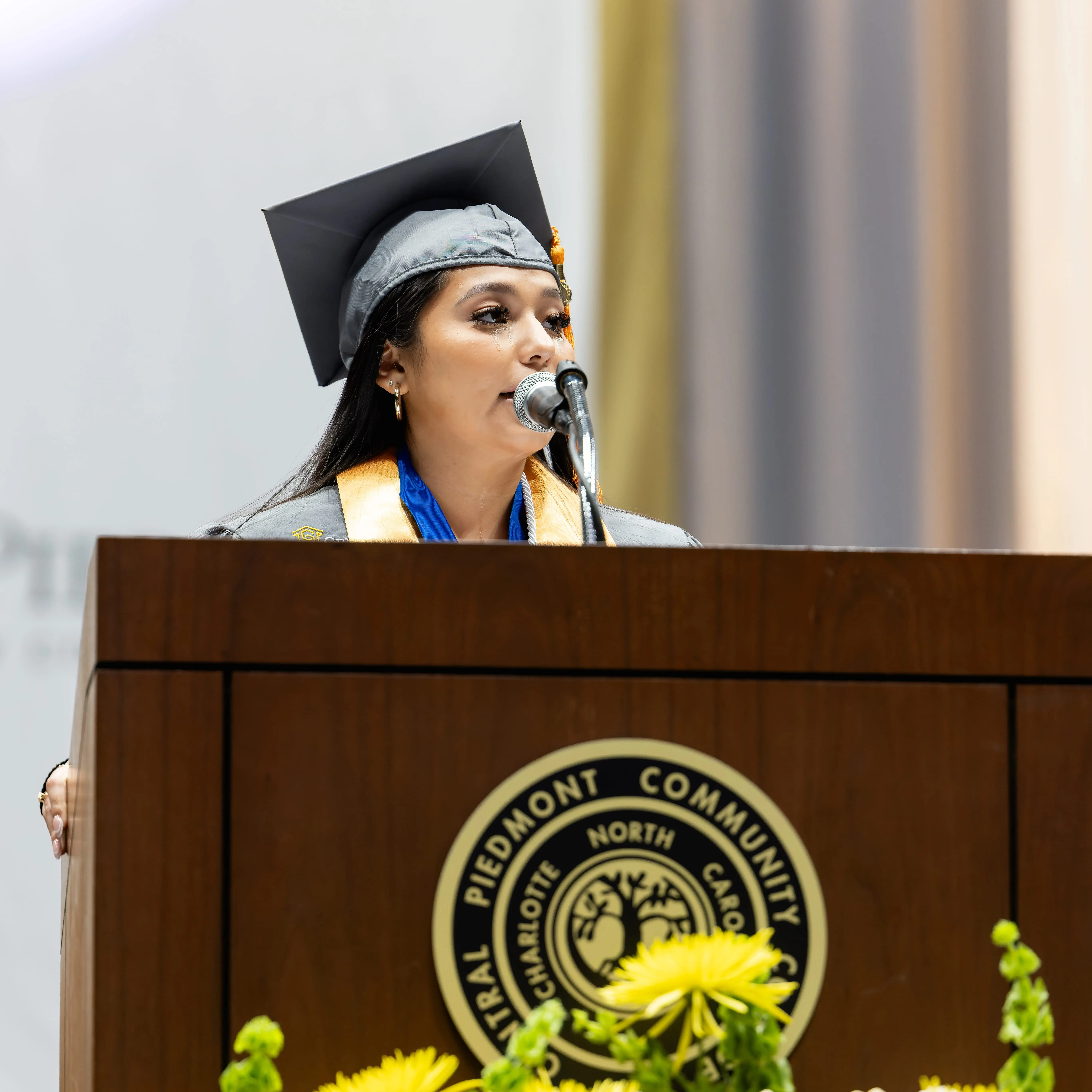 Graduate in cap and gown speaking at the commencement lectern