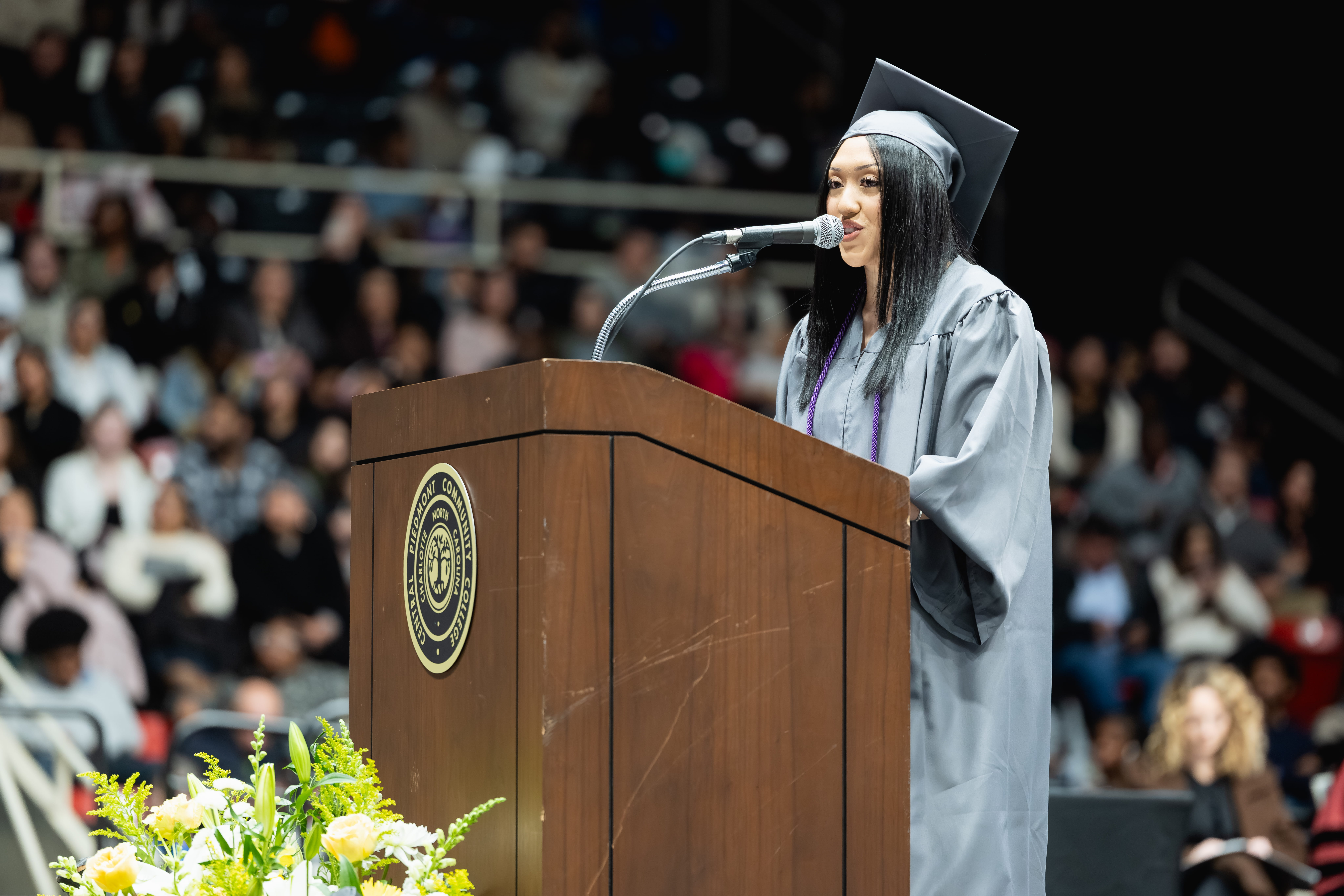 Central Piedmont student Kristen Alvarado Sorto wearing cap and gown while delivering speech at lectern at graduation.