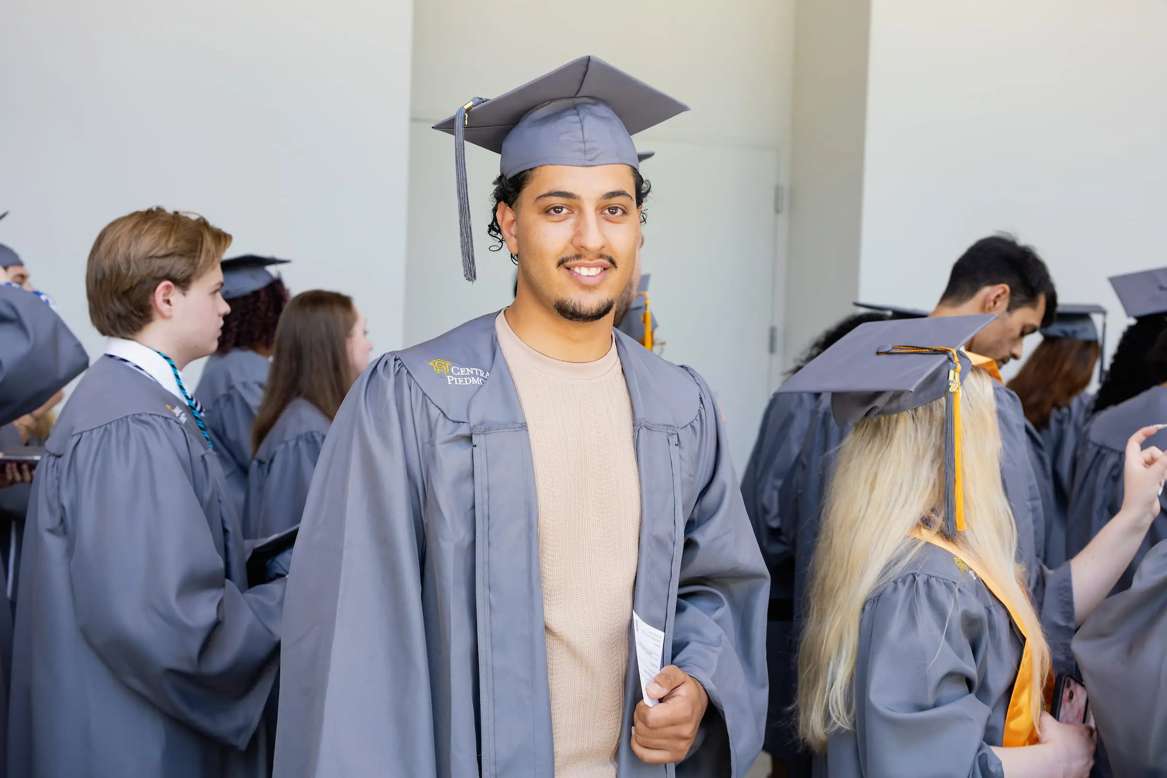 Graduate smiling in cap and gown among fellow graduates