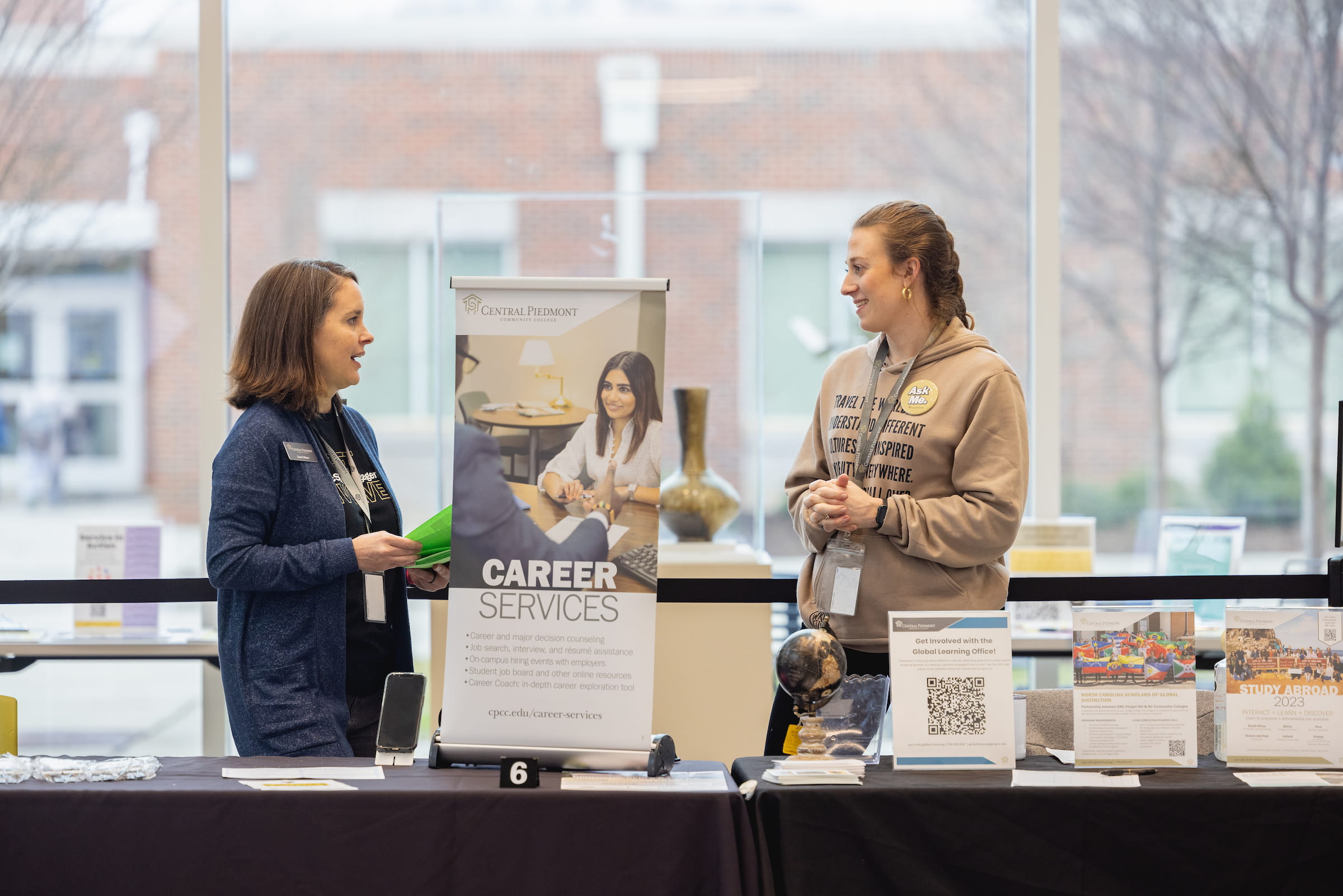 Two Central Piedmont staff members at career services booth holding information and reading materials.