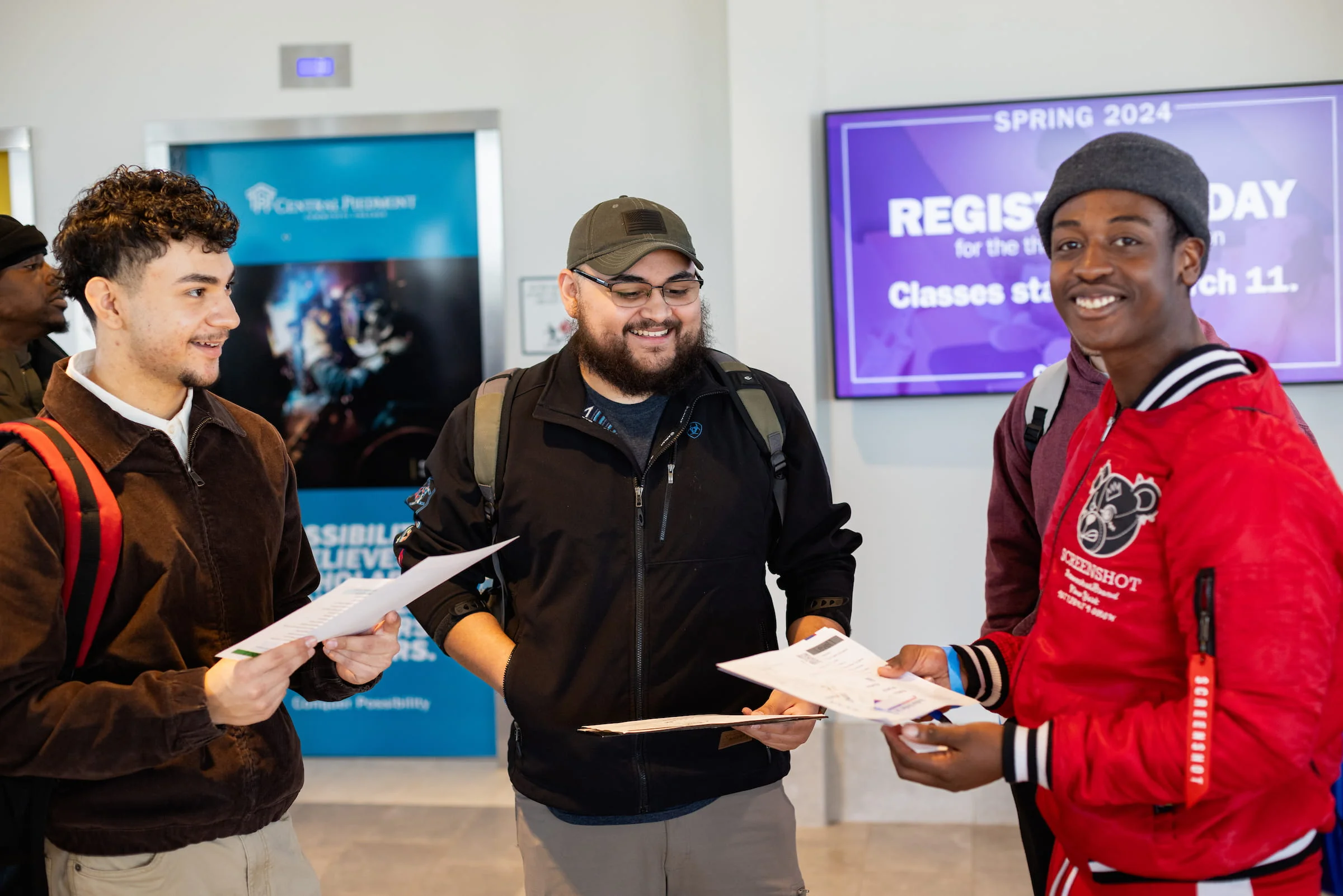 Three students holding forms in front of a registration day display