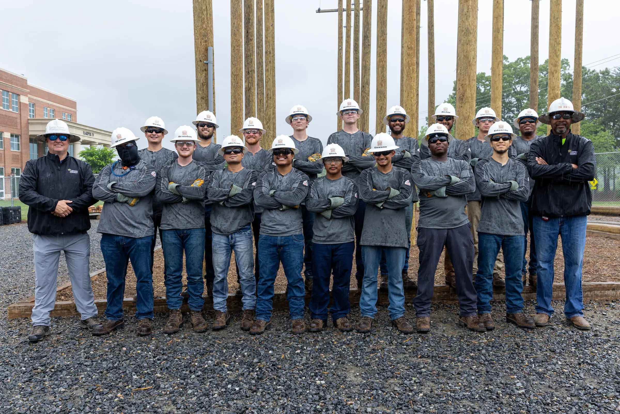 Lineworker students in hard hats lined up in front of training poles