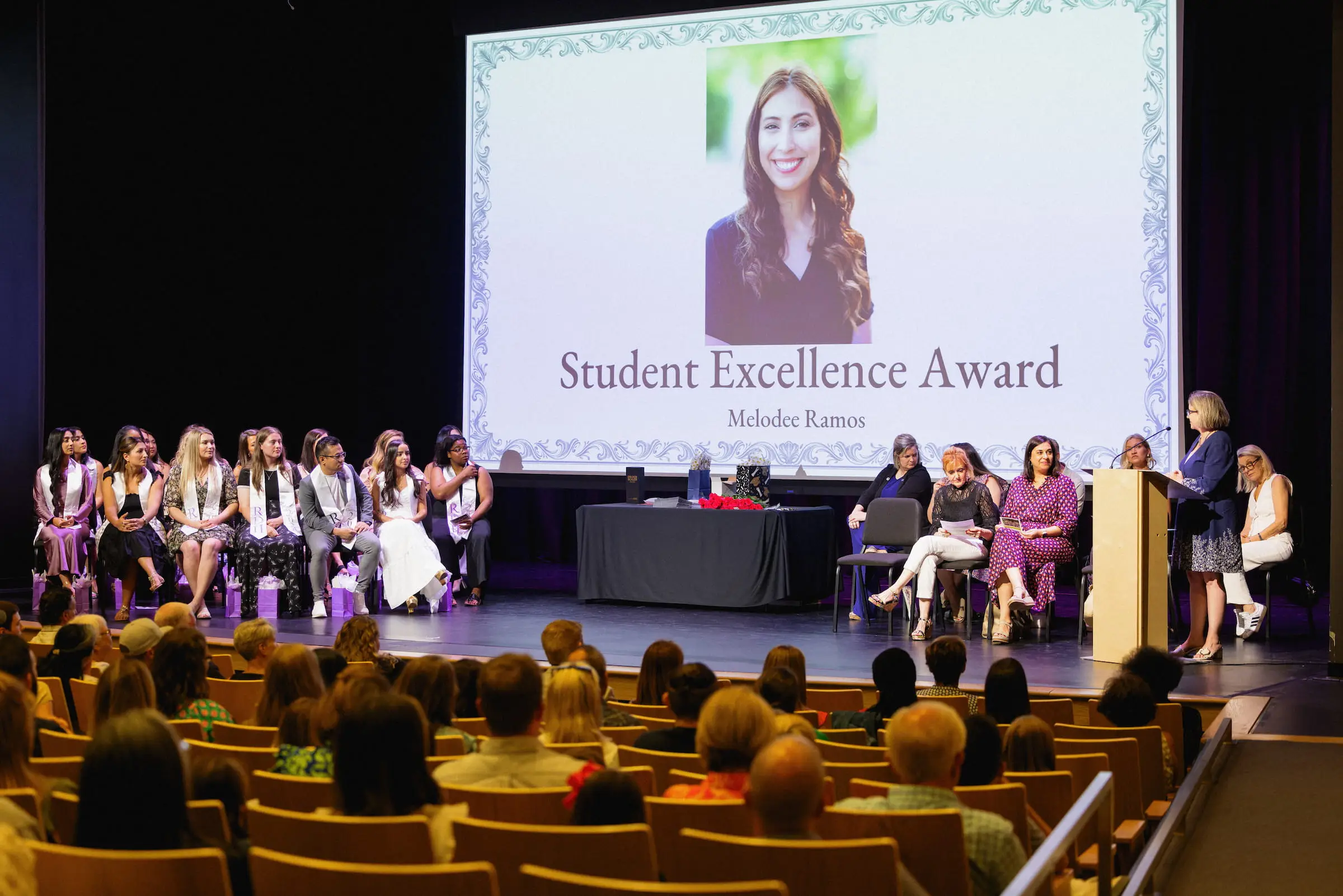 Audience at the Student Excellence Award ceremony with a recipient on screen