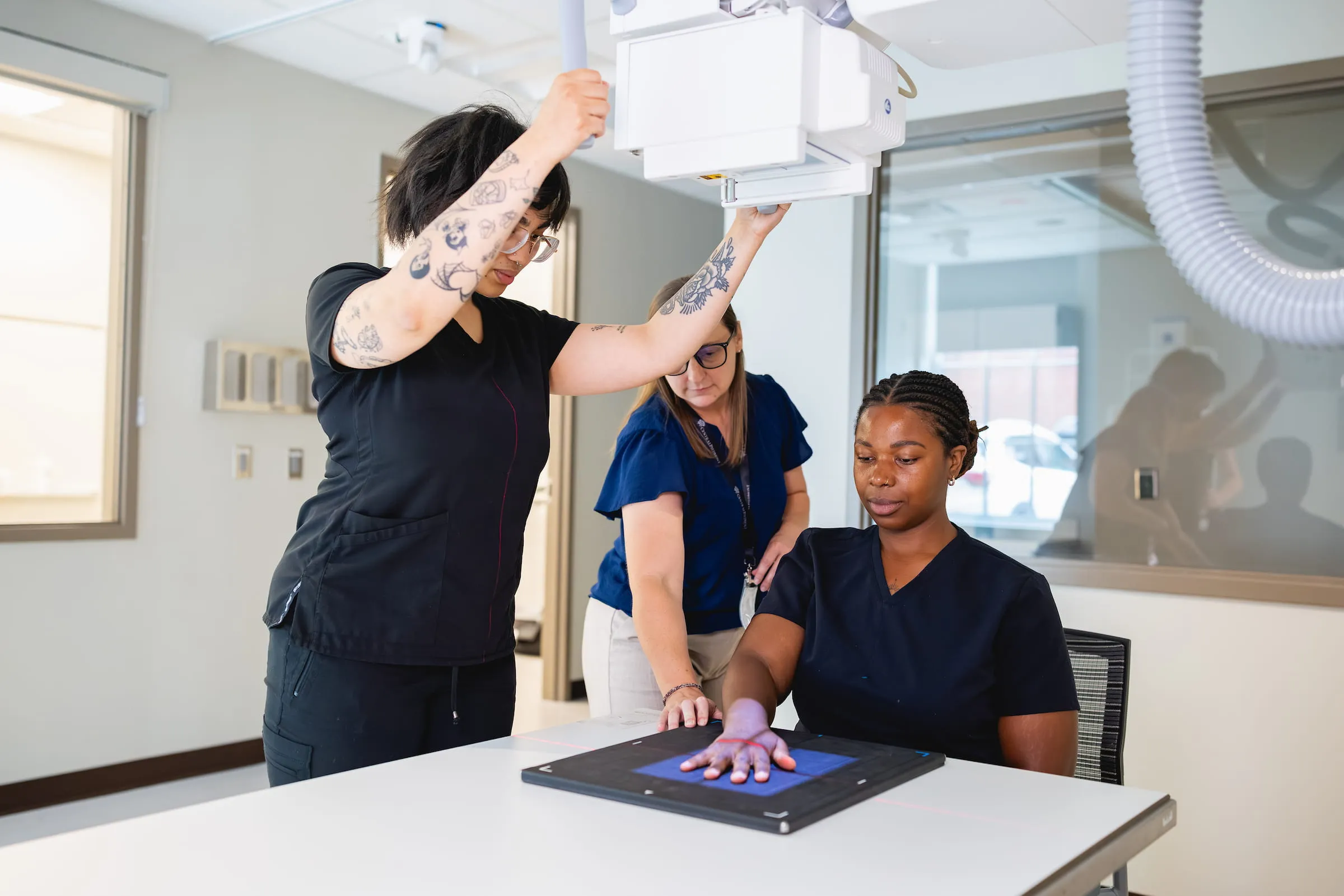 Radiography students positioning an X-ray machine over a patient's hand