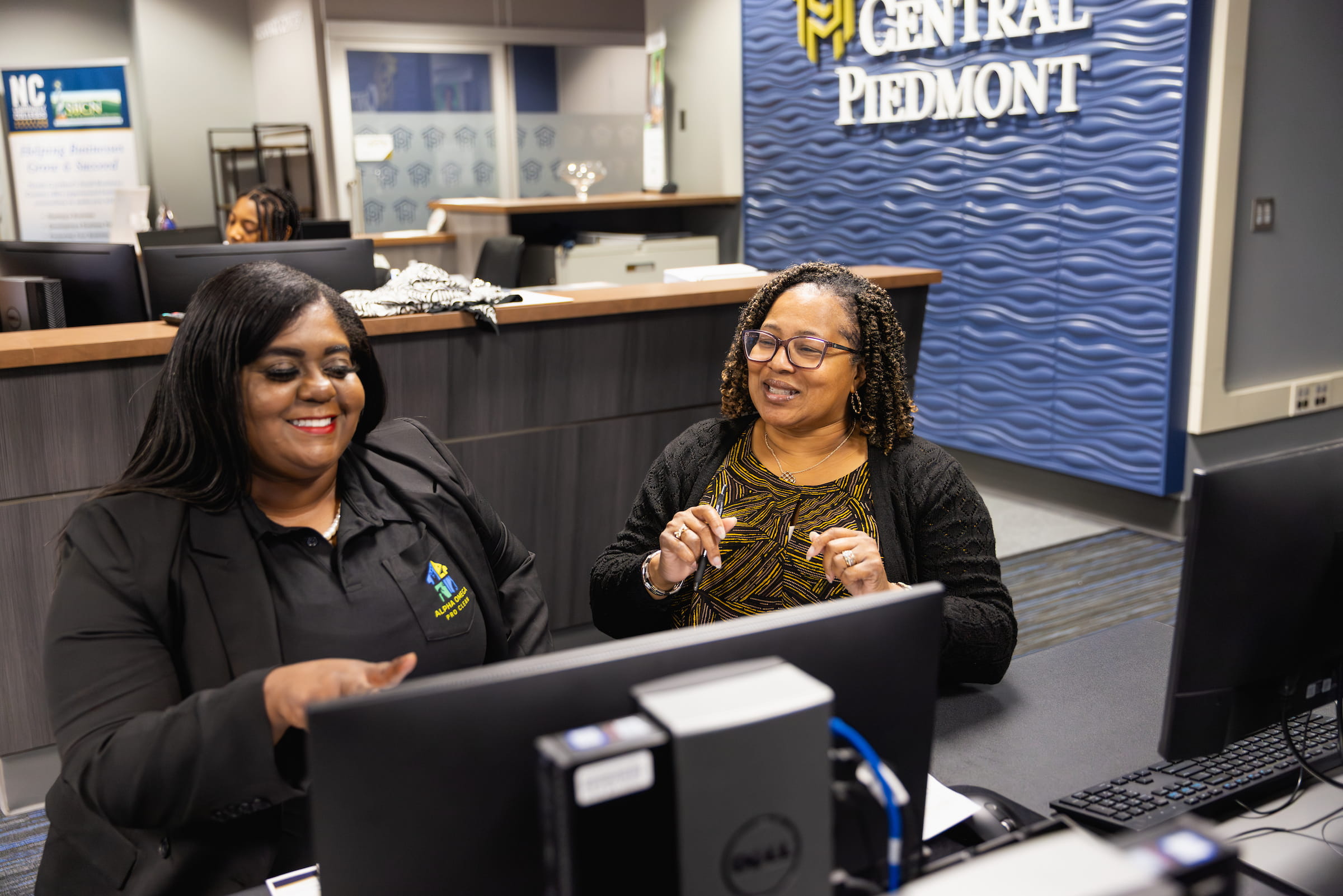 Two Central Piedmont Navigators sitting in office smiling and chatting in front of computers.