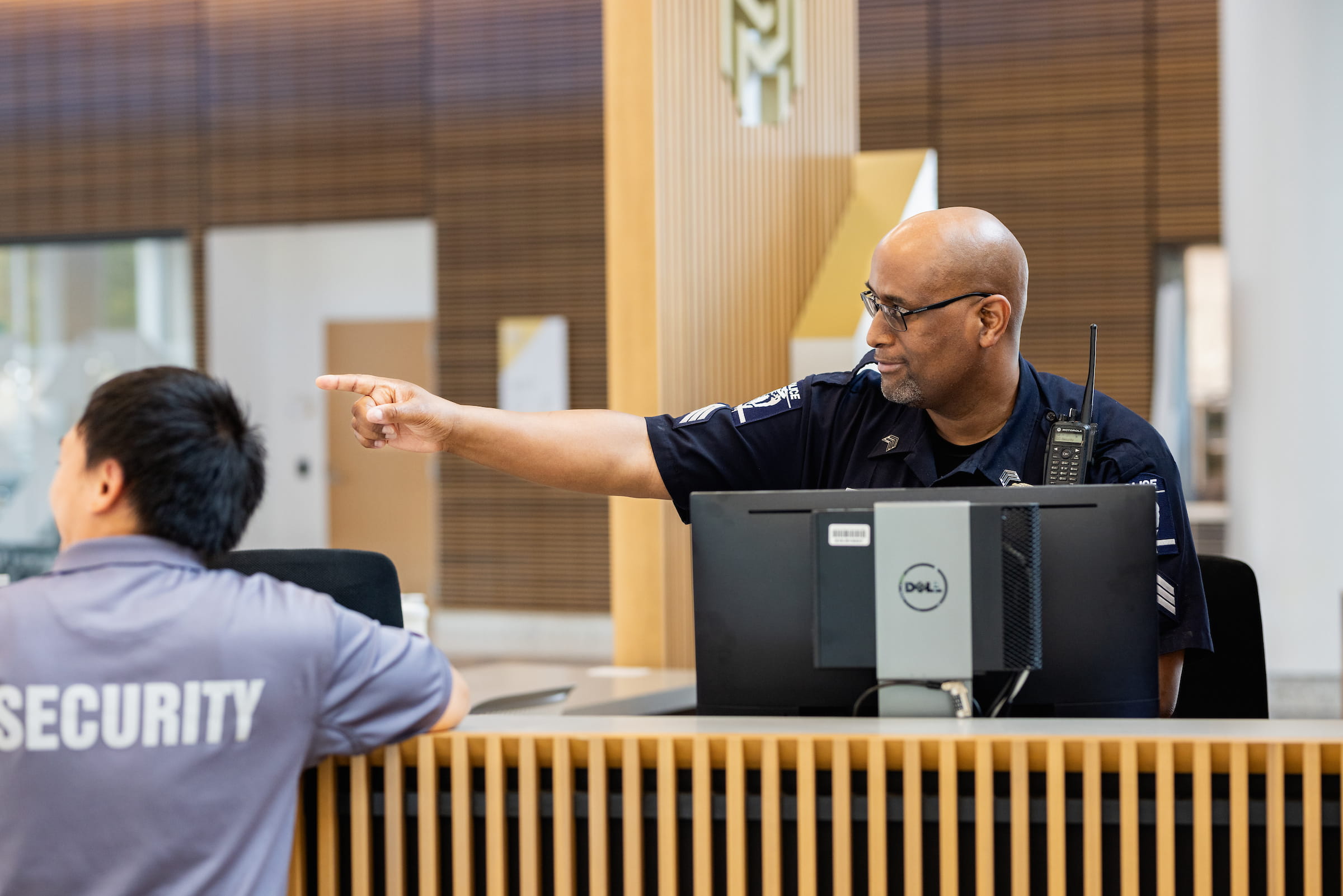 Two Central Piedmont security offers chatting at security desk with one pointing off at something in distance.