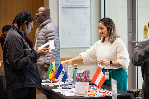 Two people standing on either side of a table with international flags.