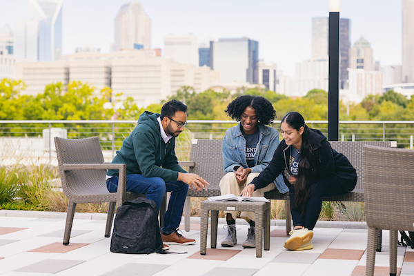 Three students talking on a rooftop terrace with the Charlotte skyline behind them
