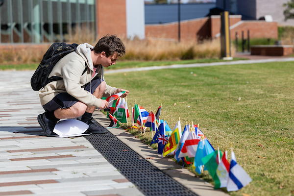 Central Piedmont student crouching next to a row of flags.