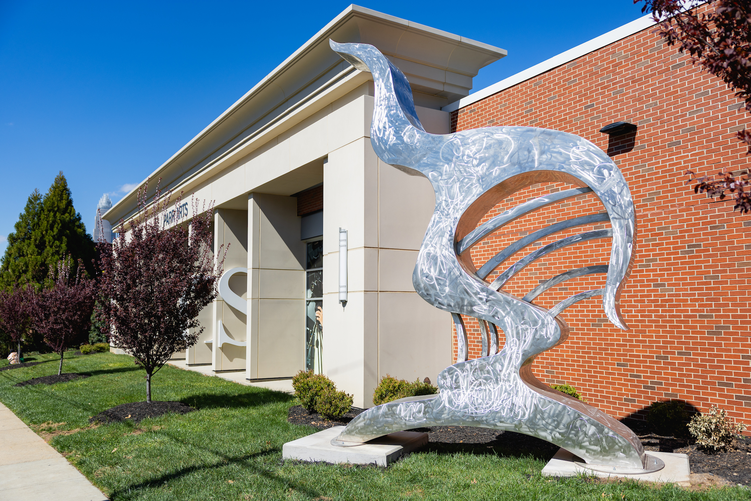 Large silver abstract sculpture on the lawn beside a campus building