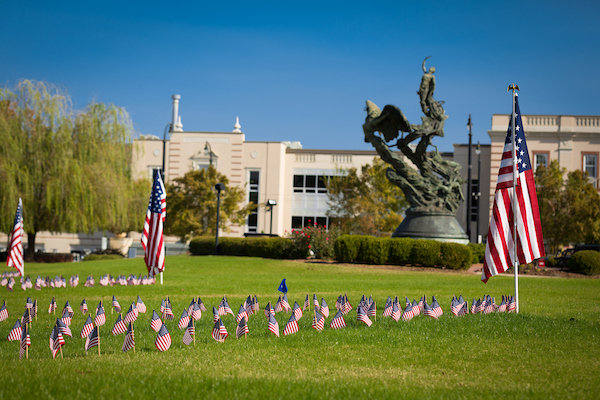 Dozens of small American flags and three large American flags in ground with Central Piedmont campus in background.