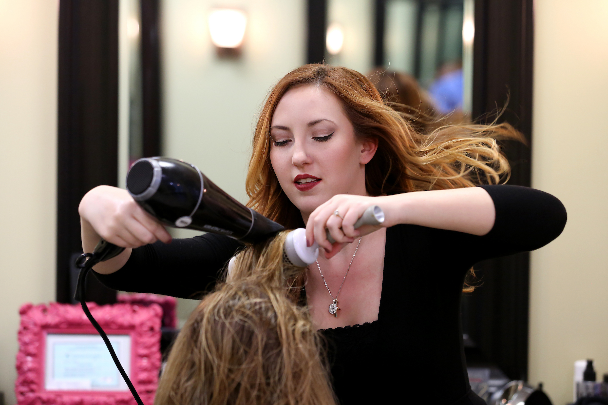 A Central Piedmont cosmetology student using a hair dryer