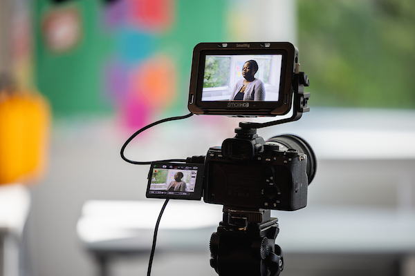 Video camera on a tripod, its viewfinder showing the person being interviewed
