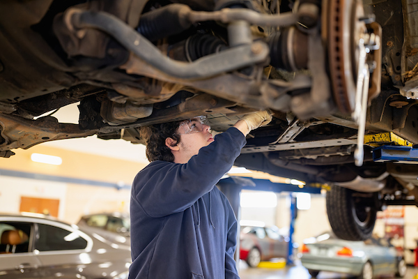 Central Piedmont Community College student inspecting the underside of a car during an auto repair course.