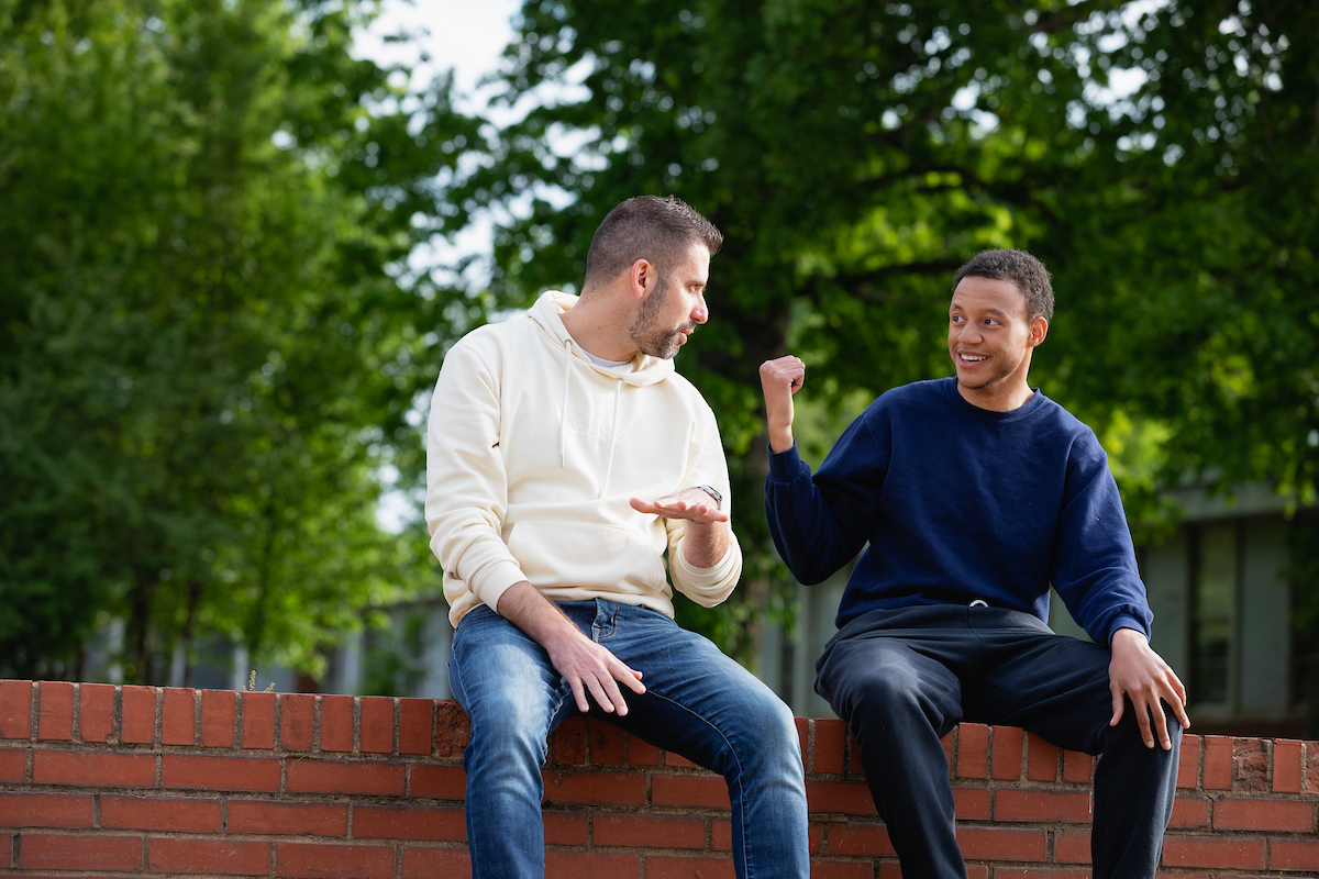 Student and advisor sitting on a brick wall and having a discussion.