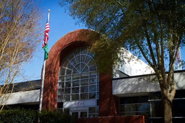 Tree casting shadow on brick WTVI building with grand brick-and-windowed entrance.