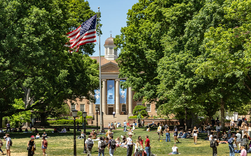 Students on a tree-shaded lawn in front of a columned building at UNC Chapel Hill