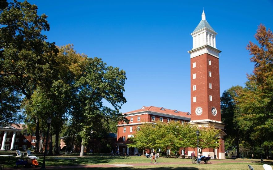 Brick clock tower rising above trees at Queens University of Charlotte