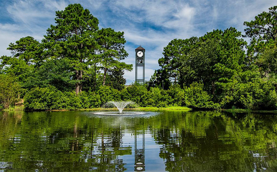 Pond and fountain framed by trees on the UNC Wilmington campus