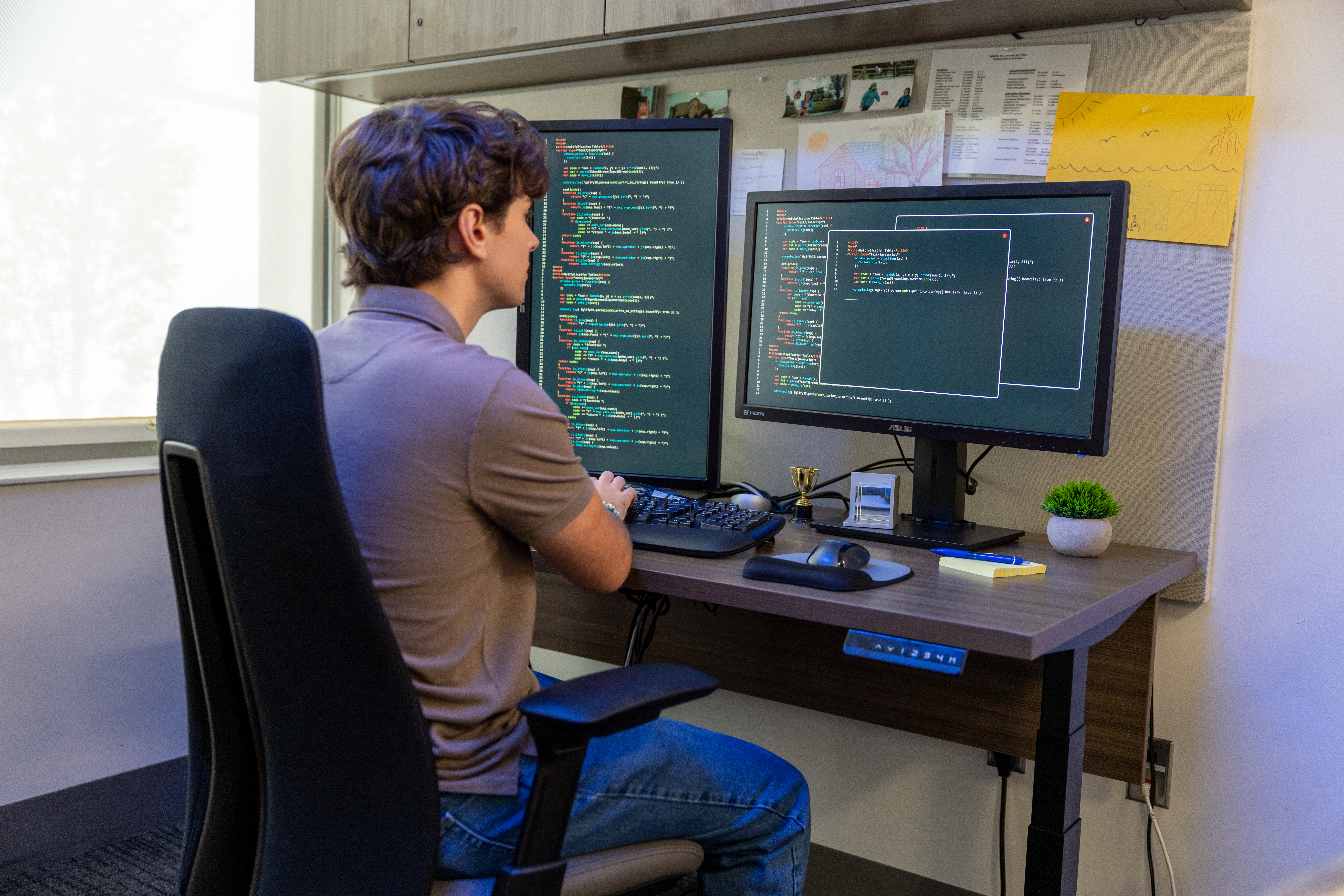 Student with his back to the camera sitting at a desk with two large monitors both with overlapping screens of code data written in green text