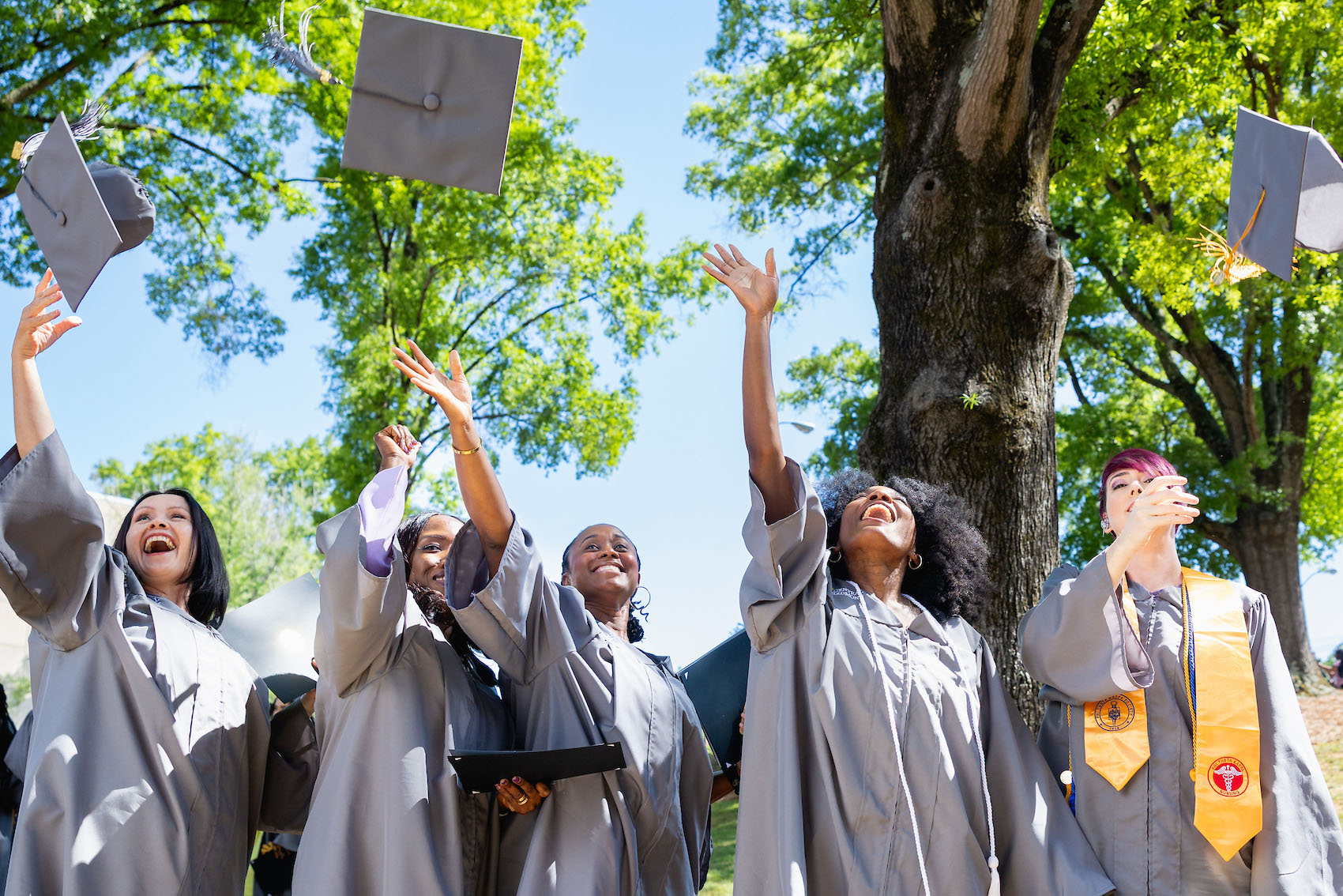 Five Central Piedmont graduates tossing their caps in the air at graduation
