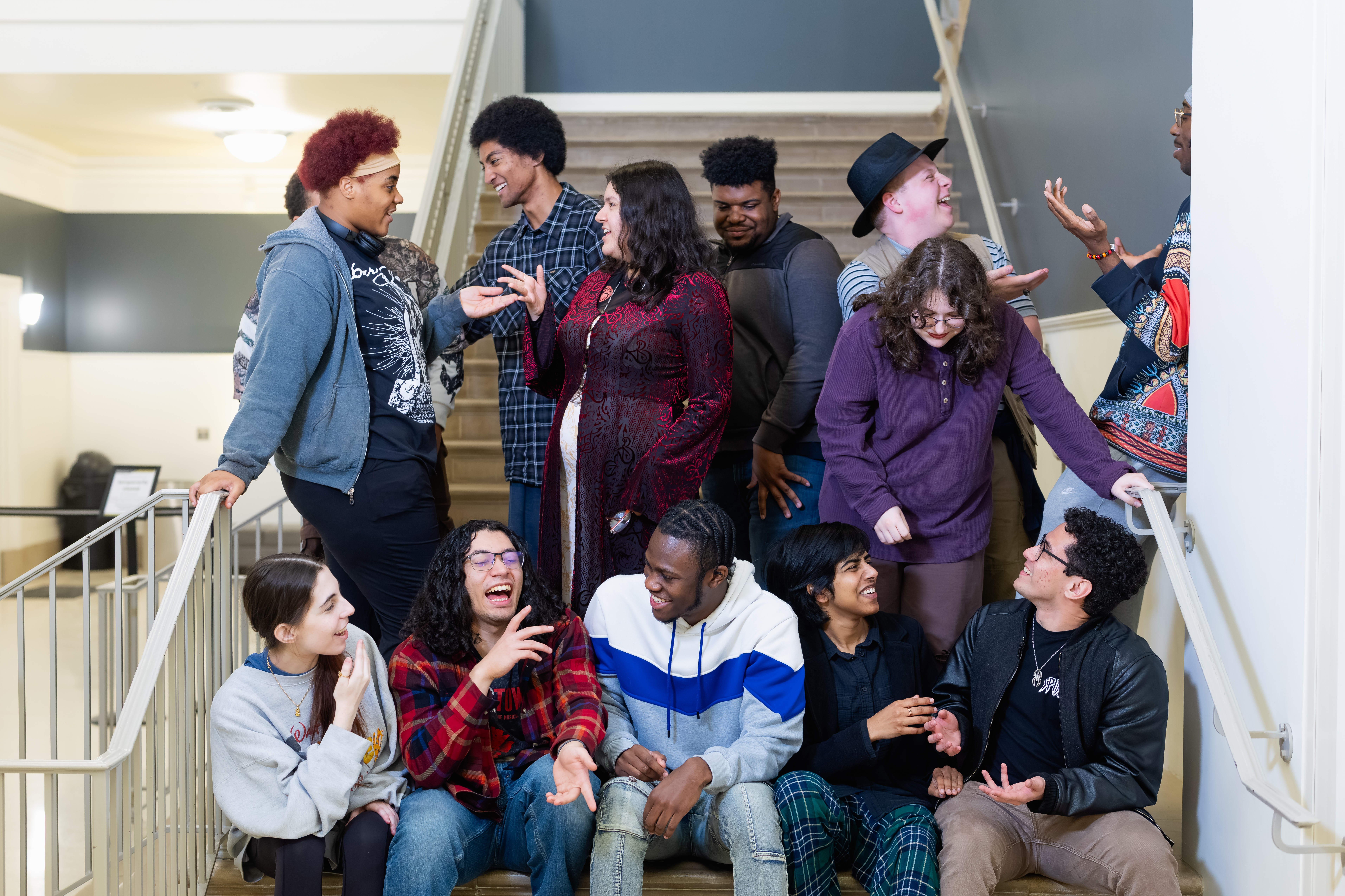 Drama students sitting on stairs laughing, gesturing and smiling to each other