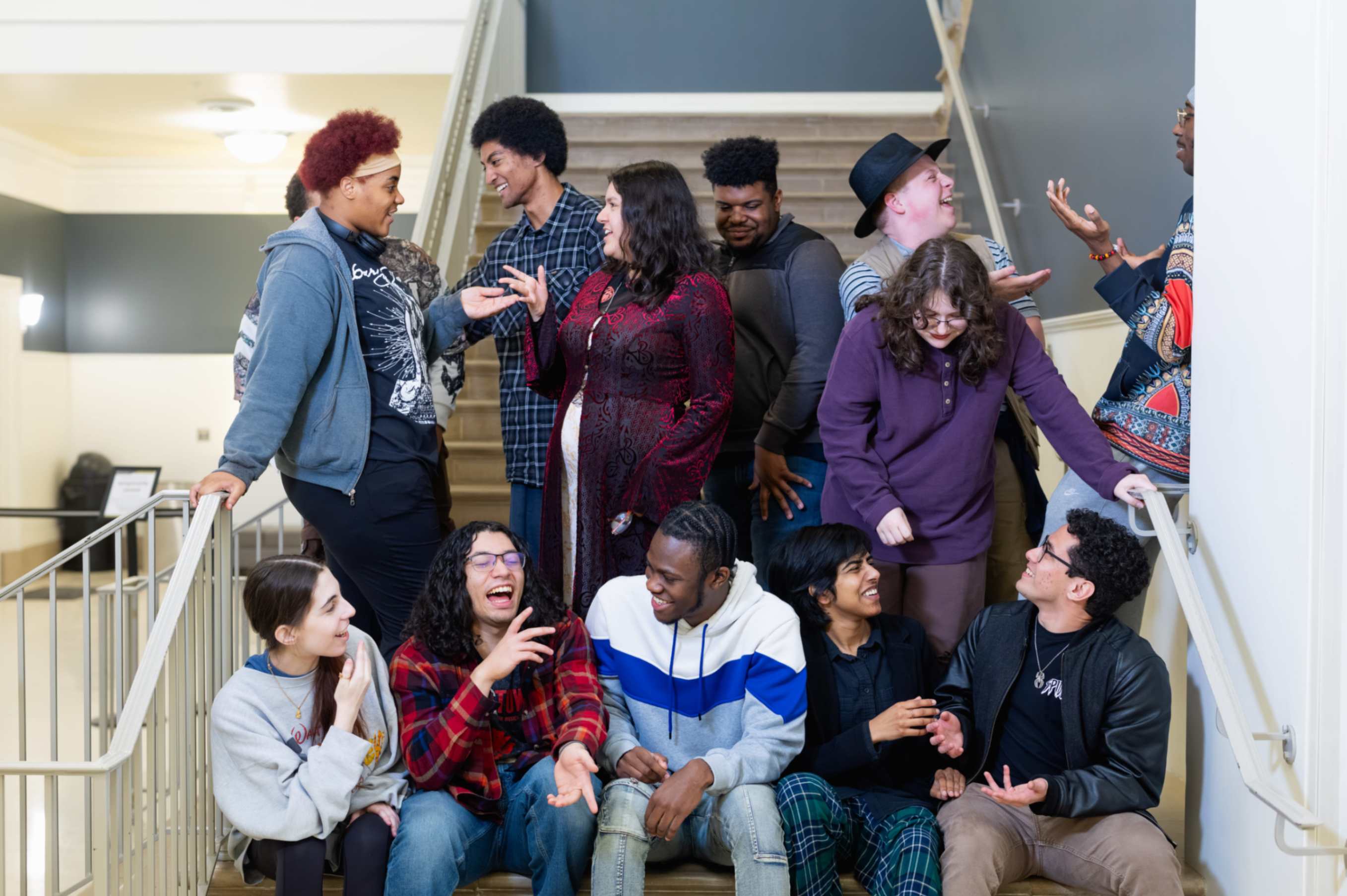 Drama students sitting on stairs laughing, gesturing and smiling to each other