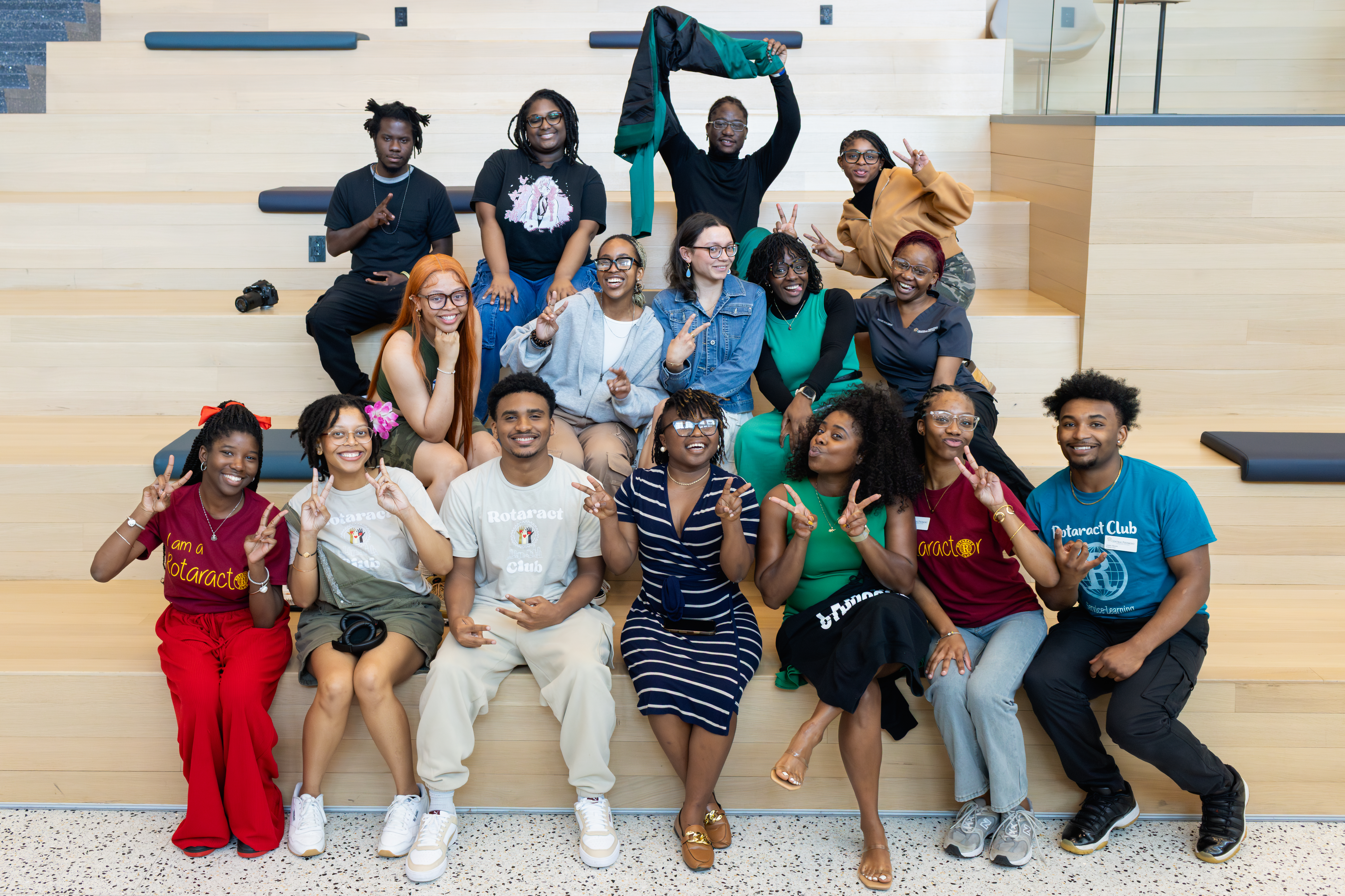 Group of students on steps in Parr Center smiling, giving peace signs with their hands and wearing Rotaract Club t-shirts